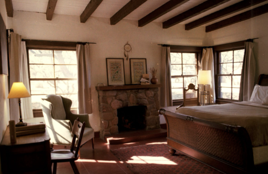 A bedroom at The Care Ranch with wooden beams, a small fireplace, and warm afternoon light
