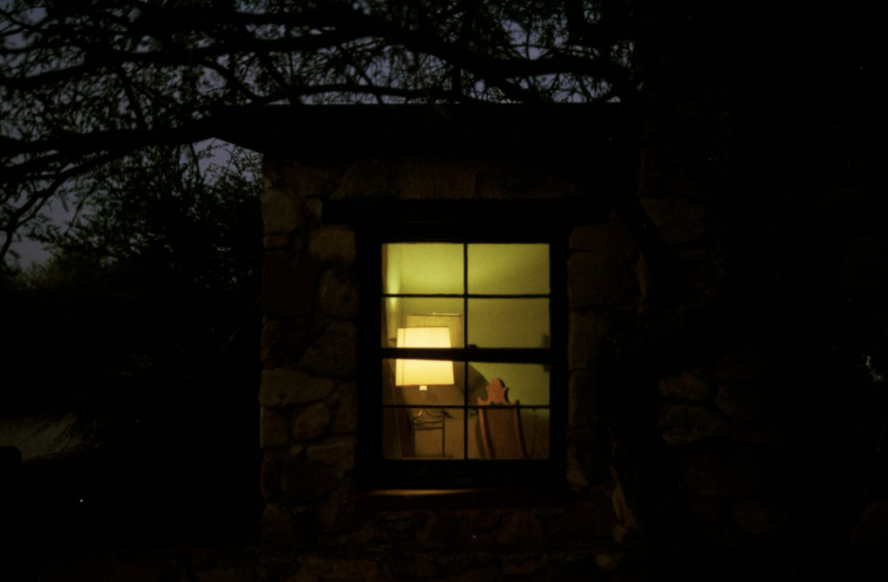 A stone guest house at night, a single window glowing with warm light